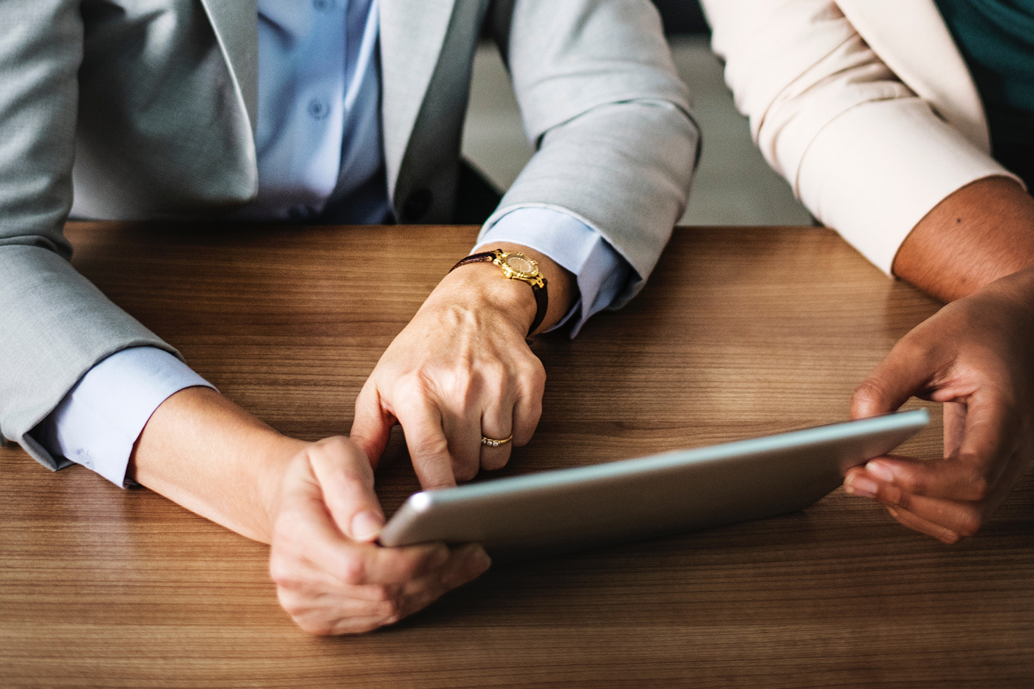 Two professionals hold a tablet computer on a wooden desk.